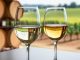 Close-up of pale-gold white wine in two glasses with soft daylight highlights and a blurred winery background.